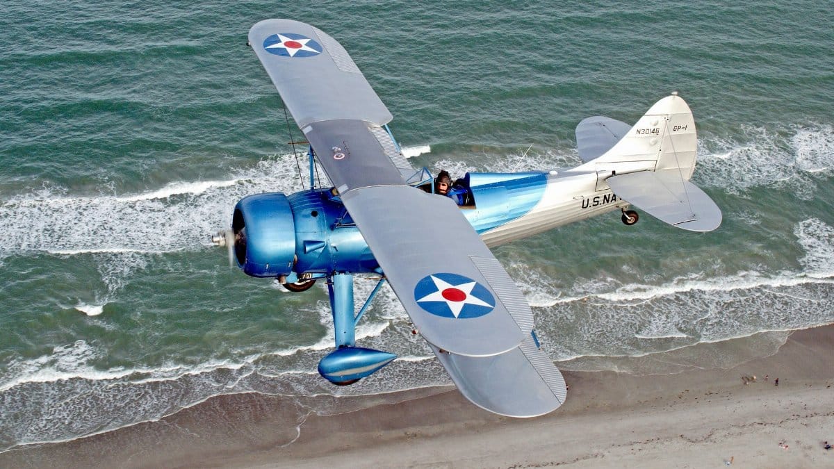 A vintage 1941 Waco biplane soars above Florida's beach, showcasing its iconic design and naval roundels.