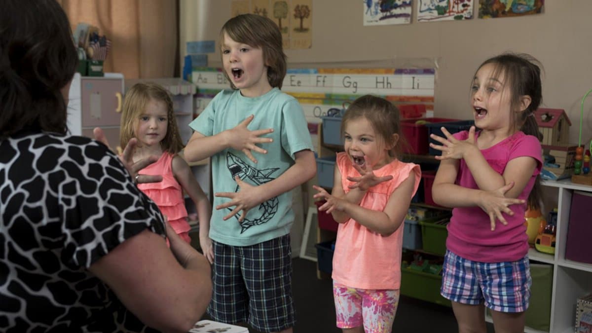 Children learning sign language with a teacher in a vibrant classroom setting.