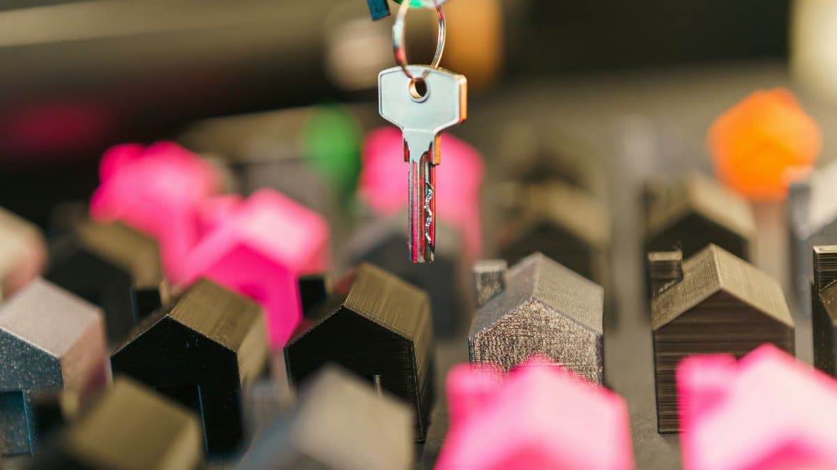 Close-up of a hand holding a key above colorful miniature houses, symbolizing real estate transaction or investment.