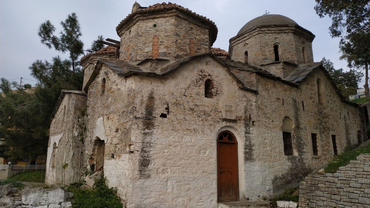 A weathered stone church with classic Byzantine architecture features an arched wooden door, captured in a serene outdoor setting.