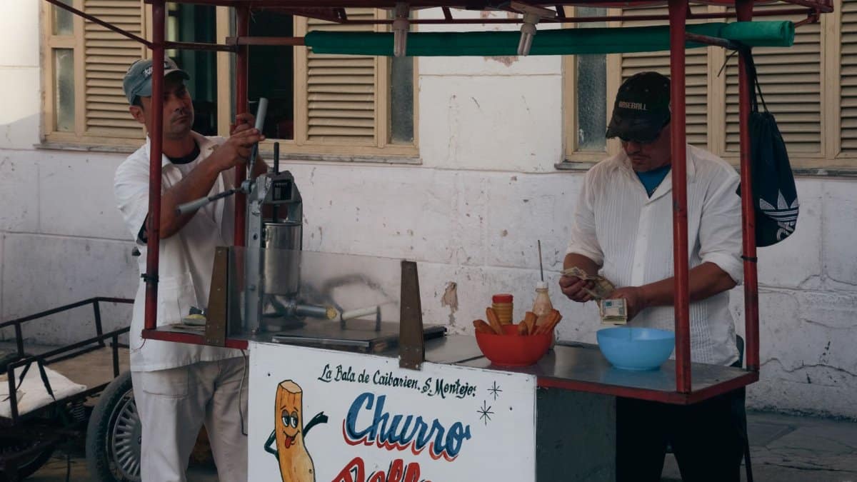 Two men operate a churro stand in a busy urban area, preparing fresh churros for customers.
