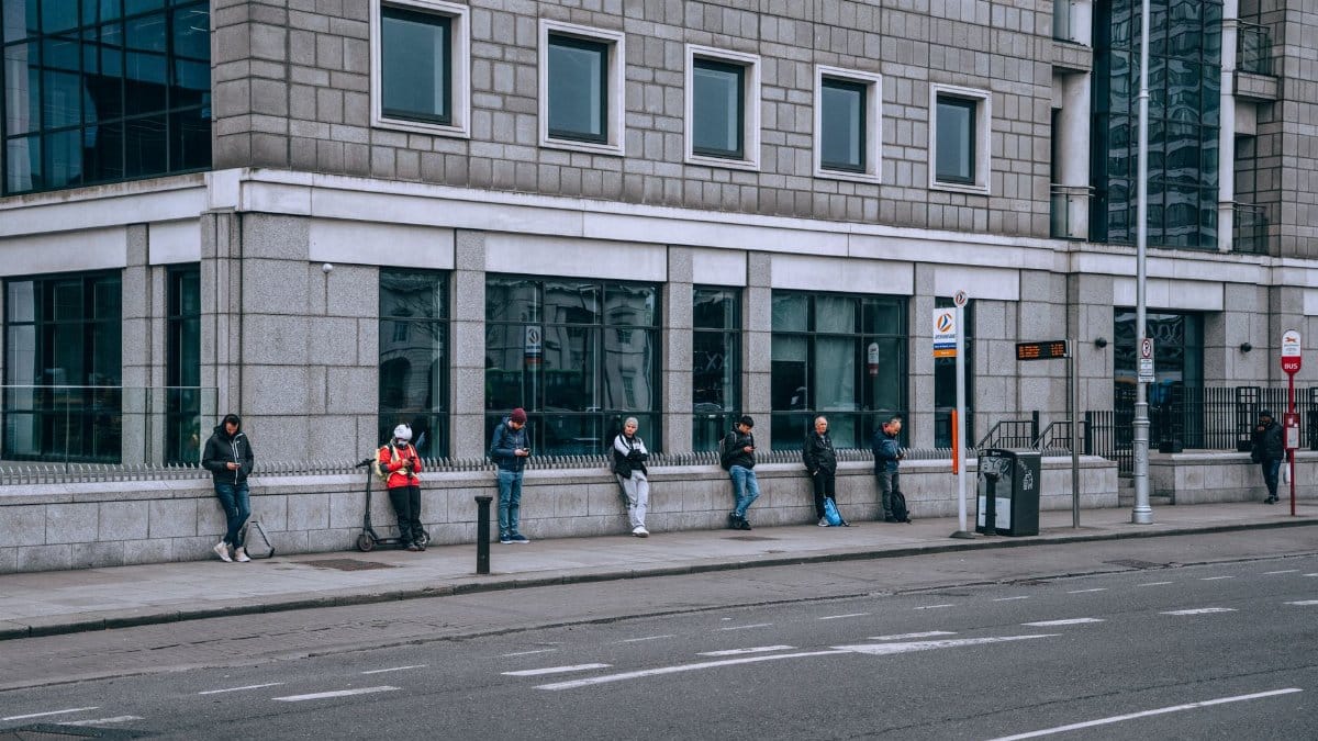 People waiting at a bus stop on a bustling city street during the day.
