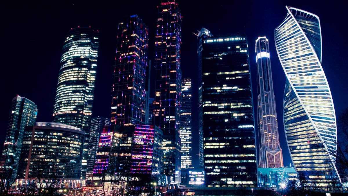 Illuminated night view of Moscow's modern skyscrapers, showcasing vibrant city lights and urban architecture.