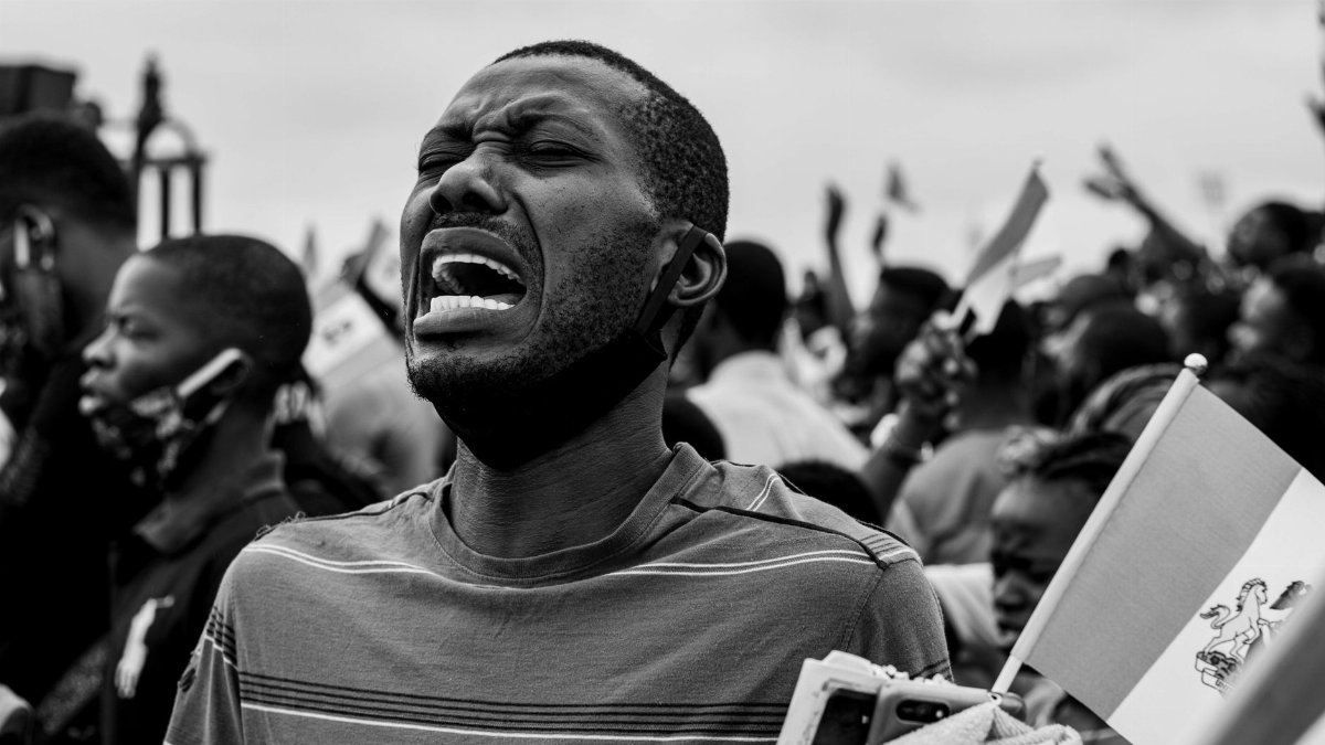 A powerful black and white photograph of a man expressing emotion during a protest, holding a flag.
