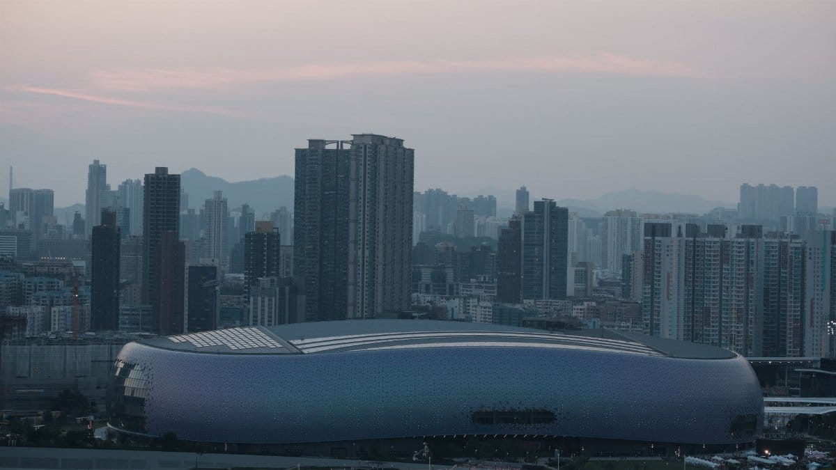 Aerial view of a city skyline with a distinctive, modern stadium and skyscrapers at twilight.
