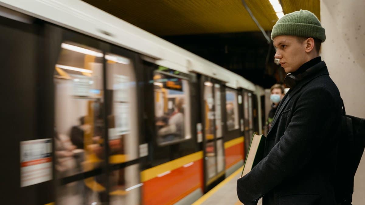 A young man stands at a busy subway station, train arriving, urban commute.