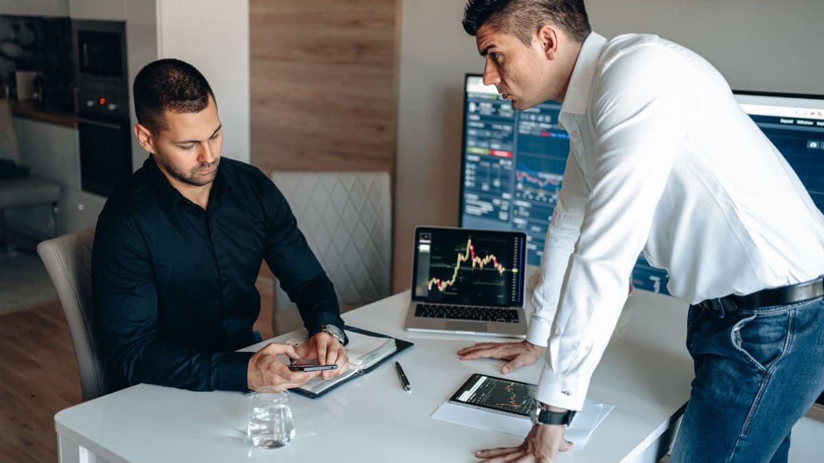 Two businessmen discussing digital market trends with laptops and tablets in a modern office.