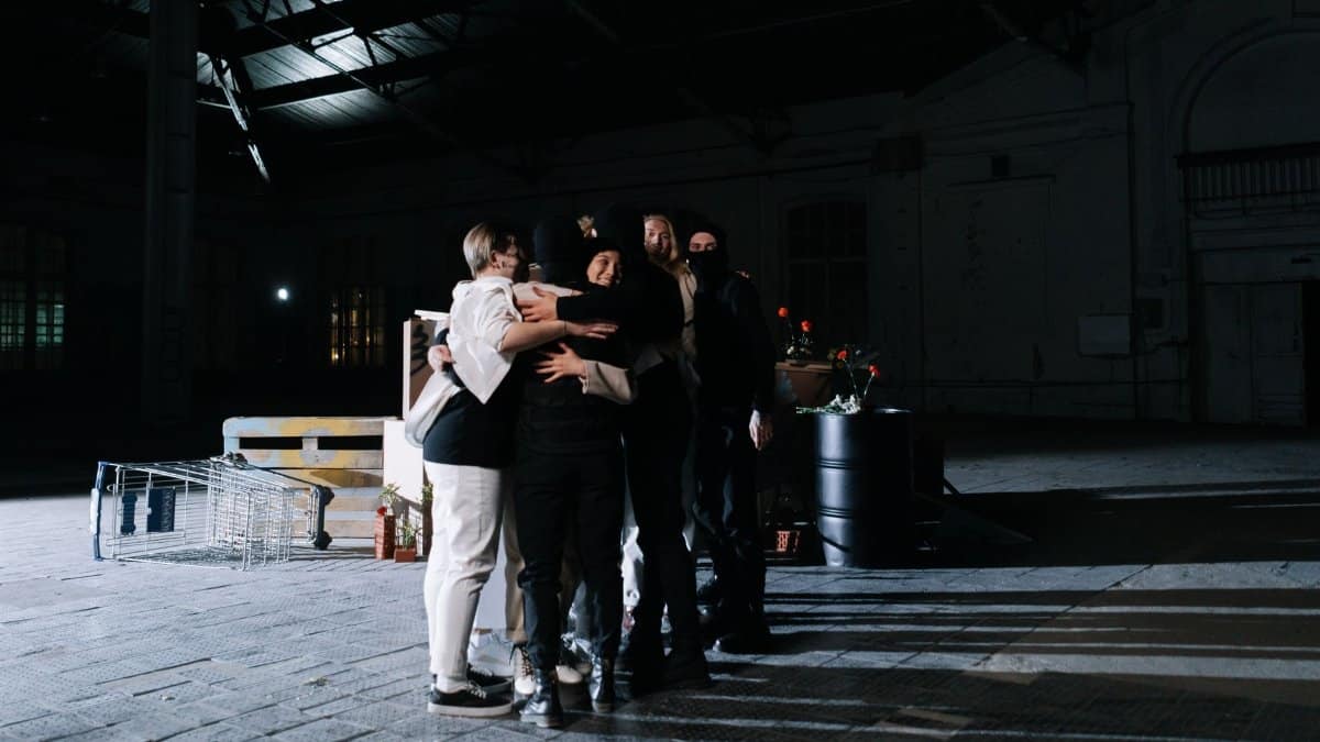 A diverse group of adults embracing in a dimly lit industrial space, symbolizing unity.