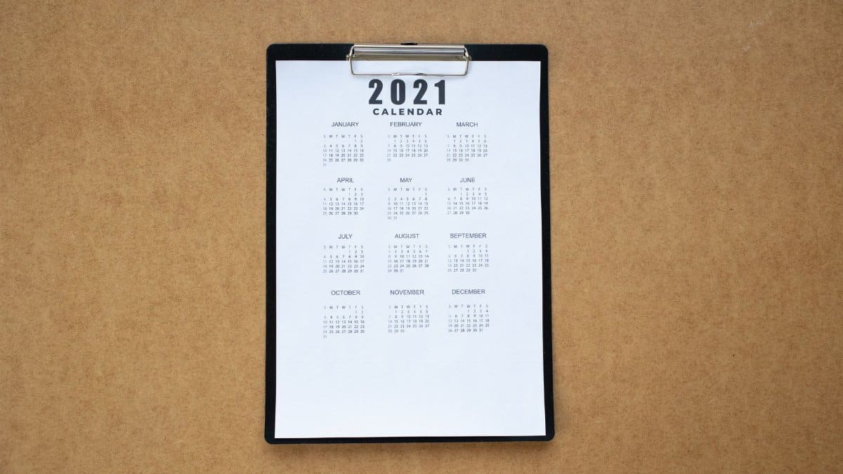 Top-down view of a minimalist 2021 calendar on a clipboard with brown background.
