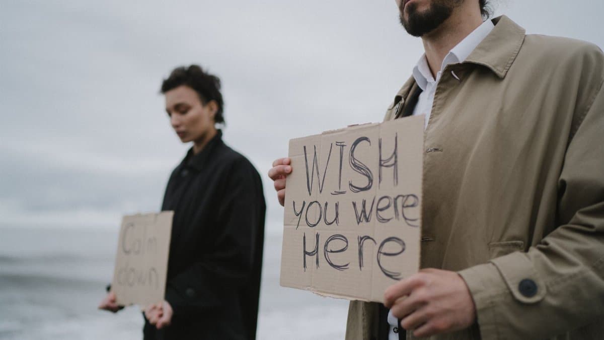 Two individuals holding cardboard signs with messages by the shore.