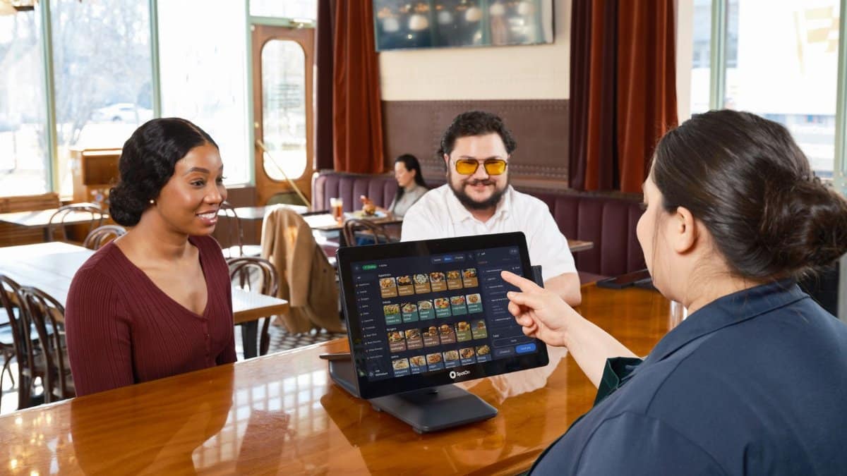 Server demonstrating a SpotOn POS system for customers in a cozy restaurant setting.