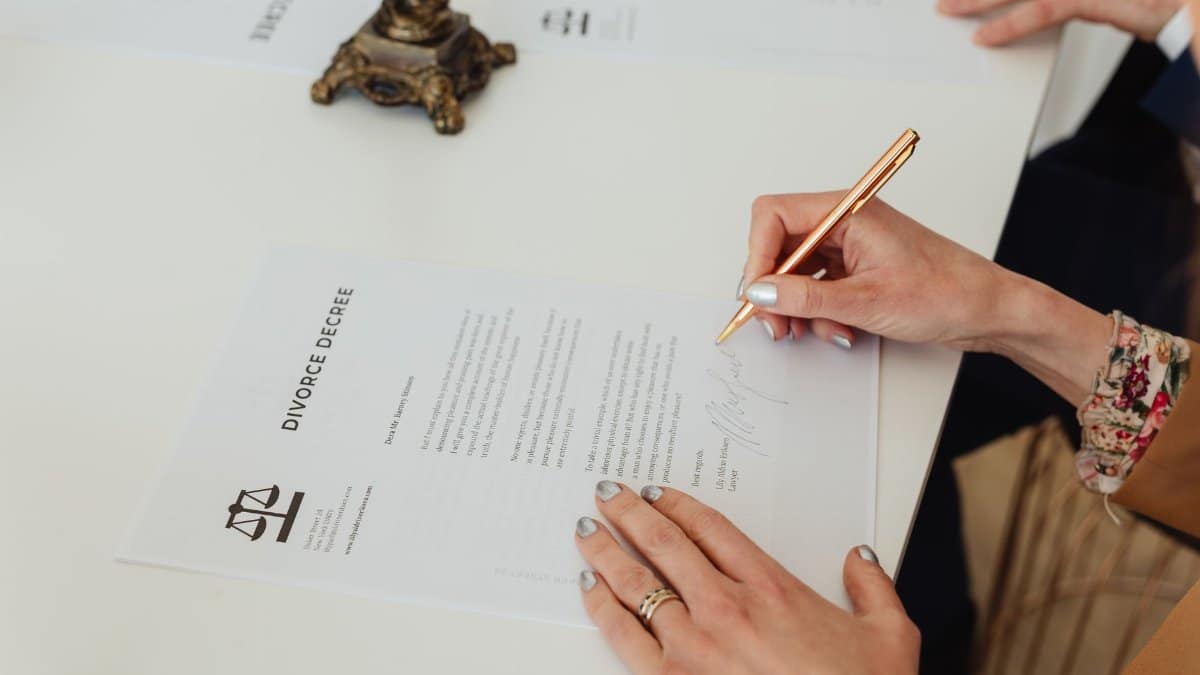 Close-up of hands signing a divorce decree document on a desk, showcasing legal process.
