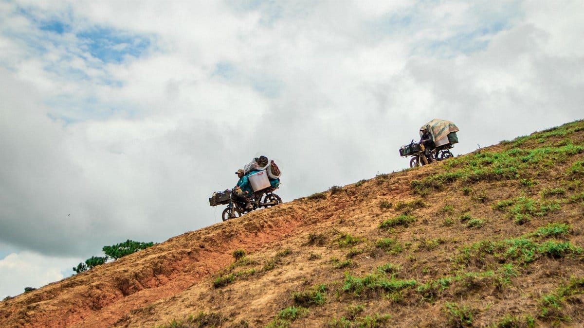 Motorcyclists carrying cargo on a steep hill in Lâm Đồng, Vietnam under a cloudy sky.