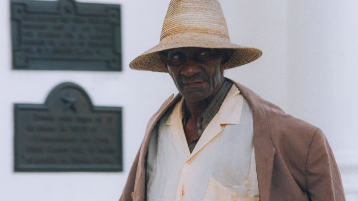 Elderly man wearing a straw hat and coat, showcasing a classic style.