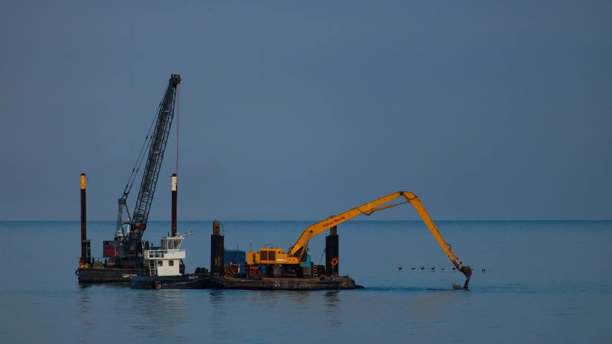 Dredging barge with crane operating at sea under clear sky.