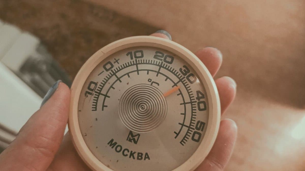 Close-up of a hand holding a vintage Moscow thermometer displaying temperature.