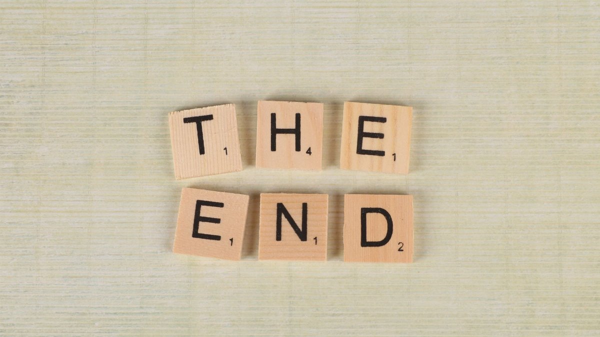 Close-up of Scrabble tiles spelling 'The End' on a simple wooden background for creative concepts.
