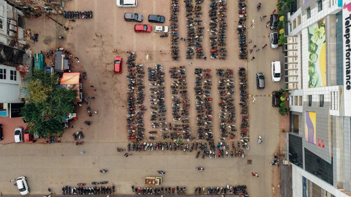 Drone shot capturing parked motorcycles and cars in a busy urban parking lot.