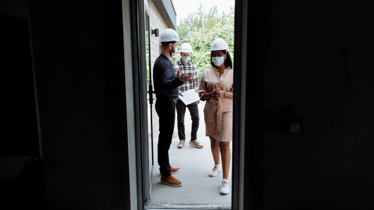 Real estate agents discussing a property at a construction site with safety measures in place.