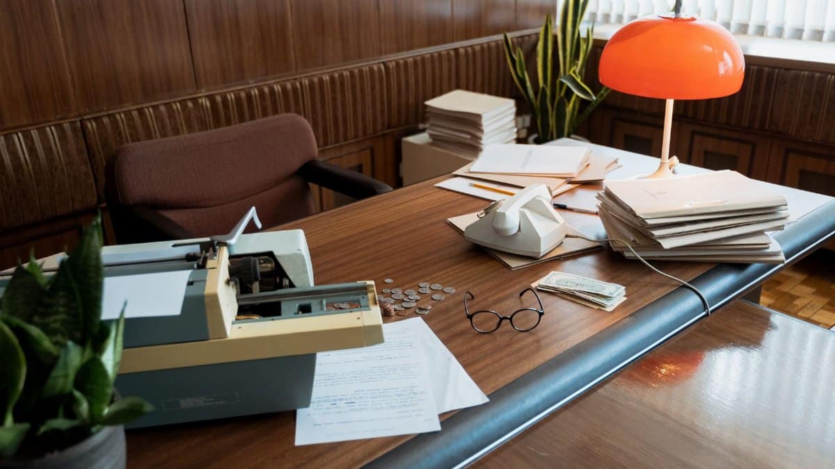 A retro office desk featuring a typewriter, vintage telephone, and stacks of documents.