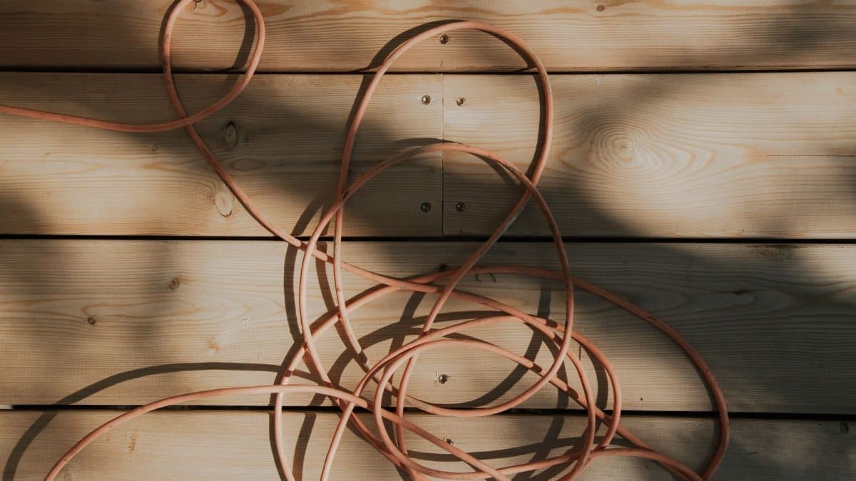 An orange cable is tangled on a sunlit wooden plank surface with shadows, creating a rustic and artistic look.