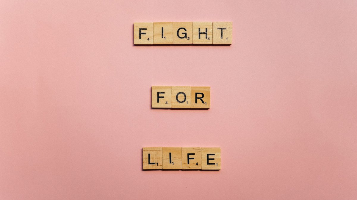 Scrabble tiles spell 'Fight for Life' on a light pink background, conveying a motivational message.