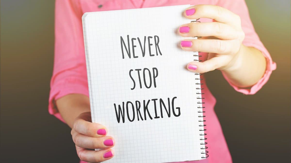 A woman holding a notebook with the motivational message 'Never Stop Working' indoors.