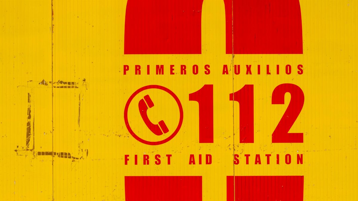 Bright yellow and red emergency sign indicating first aid station. Call 112 for emergencies.