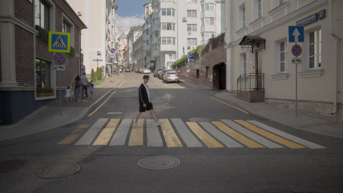 A person crosses a city street at a pedestrian lane with cars and buildings around.