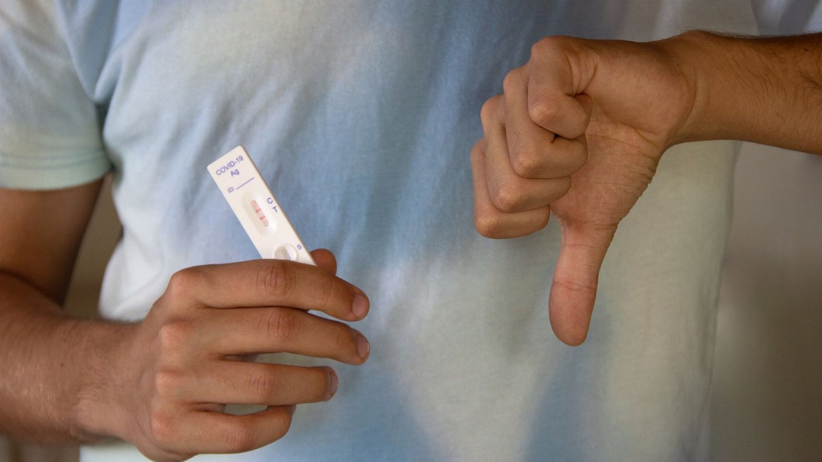 Person holding a negative COVID-19 antigen test showing a thumbs down gesture.