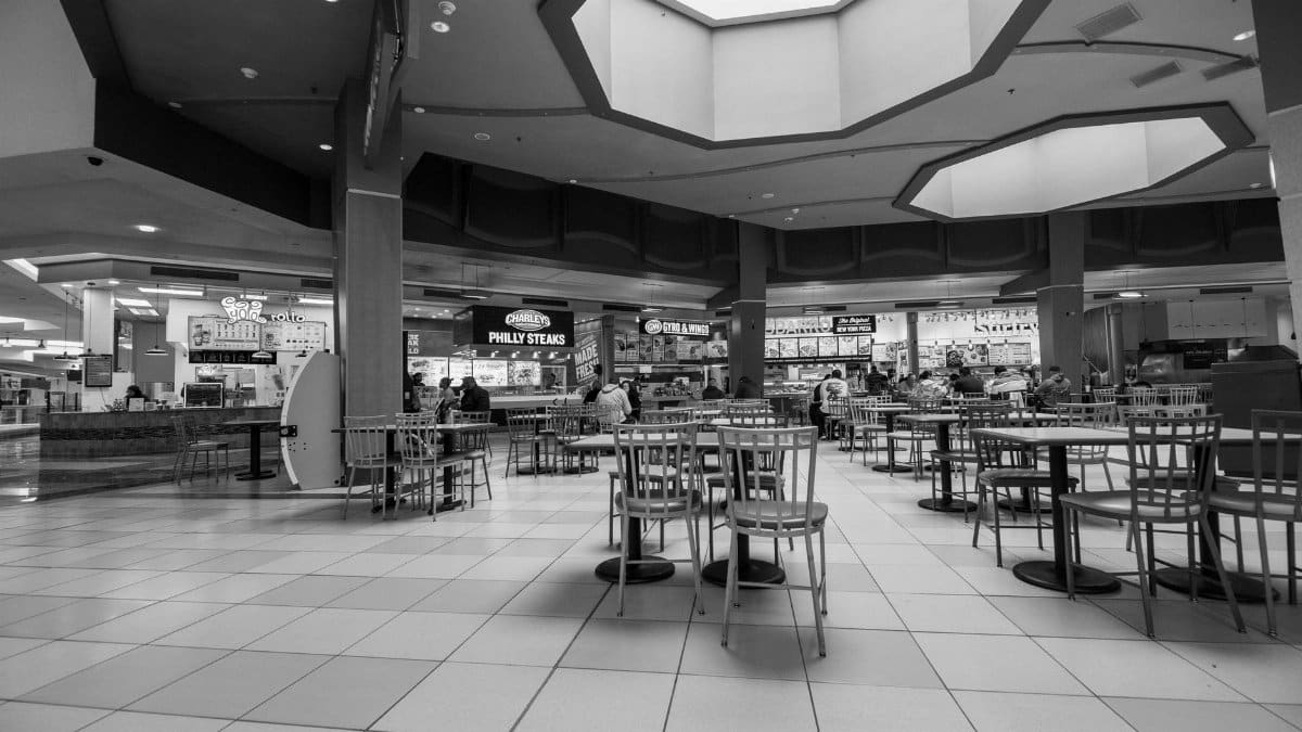 Empty chairs and tables in a food court with fast food restaurants in the background.