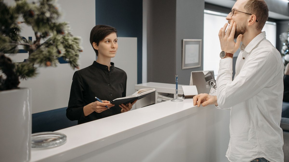 A receptionist assists a patient with a toothache at a dental clinic's front desk.