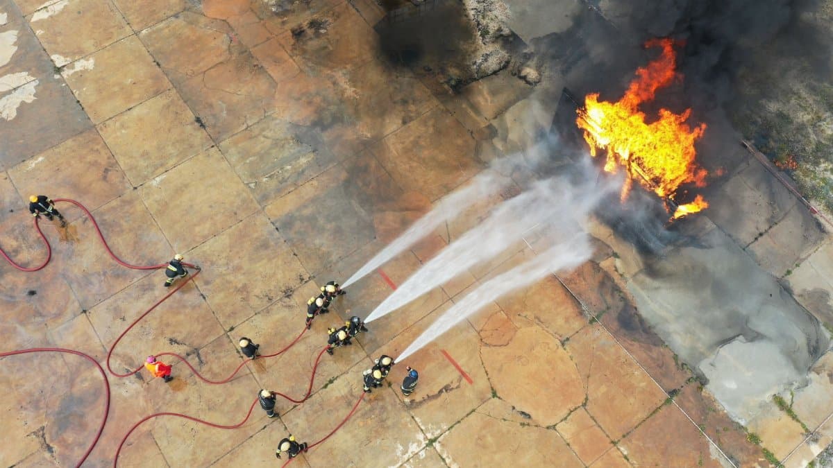 Aerial view of firefighters controlling a fire during a training exercise. Thick smoke and bright flames present.