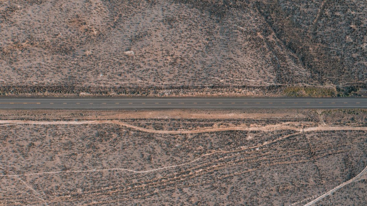 An aerial view capturing a straight road cutting through a barren desert landscape, showcasing solitude and vastness.