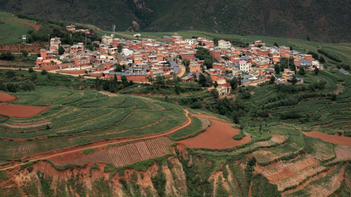 Aerial shot of a picturesque rural village surrounded by lush terraced fields in a valley.