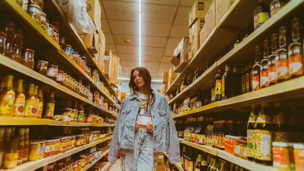 Woman in denim browsing grocery store aisle with products on shelves.