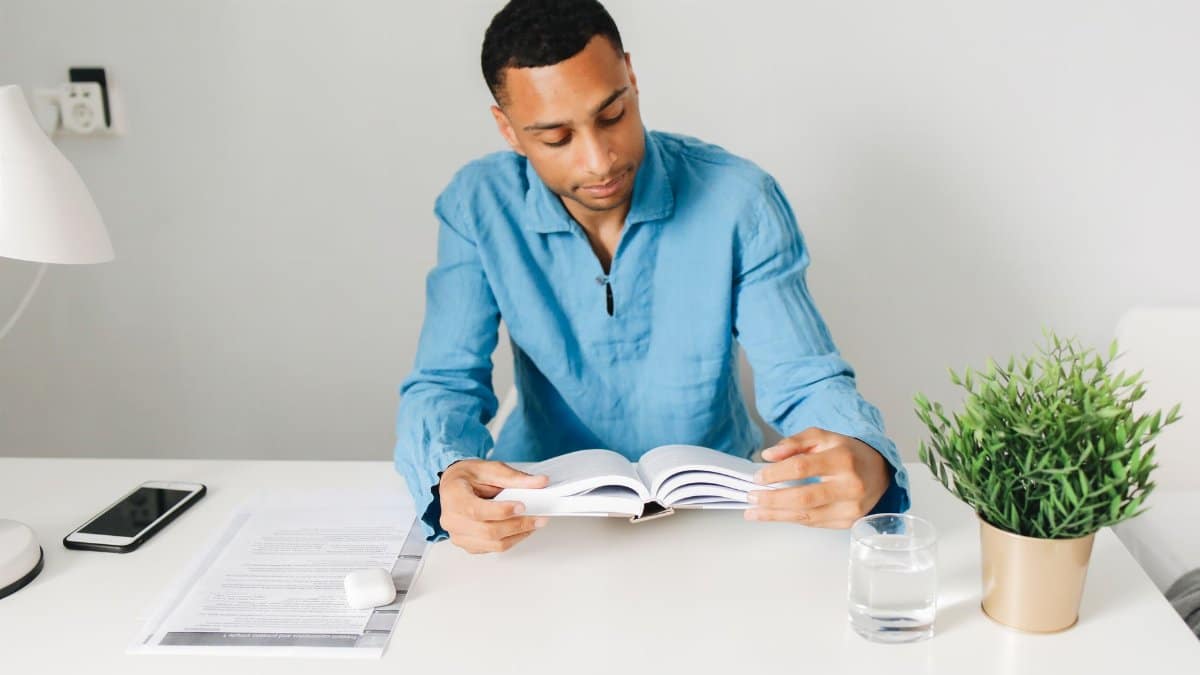 Young man studying with a book at a modern desk. Calm and focused atmosphere.
