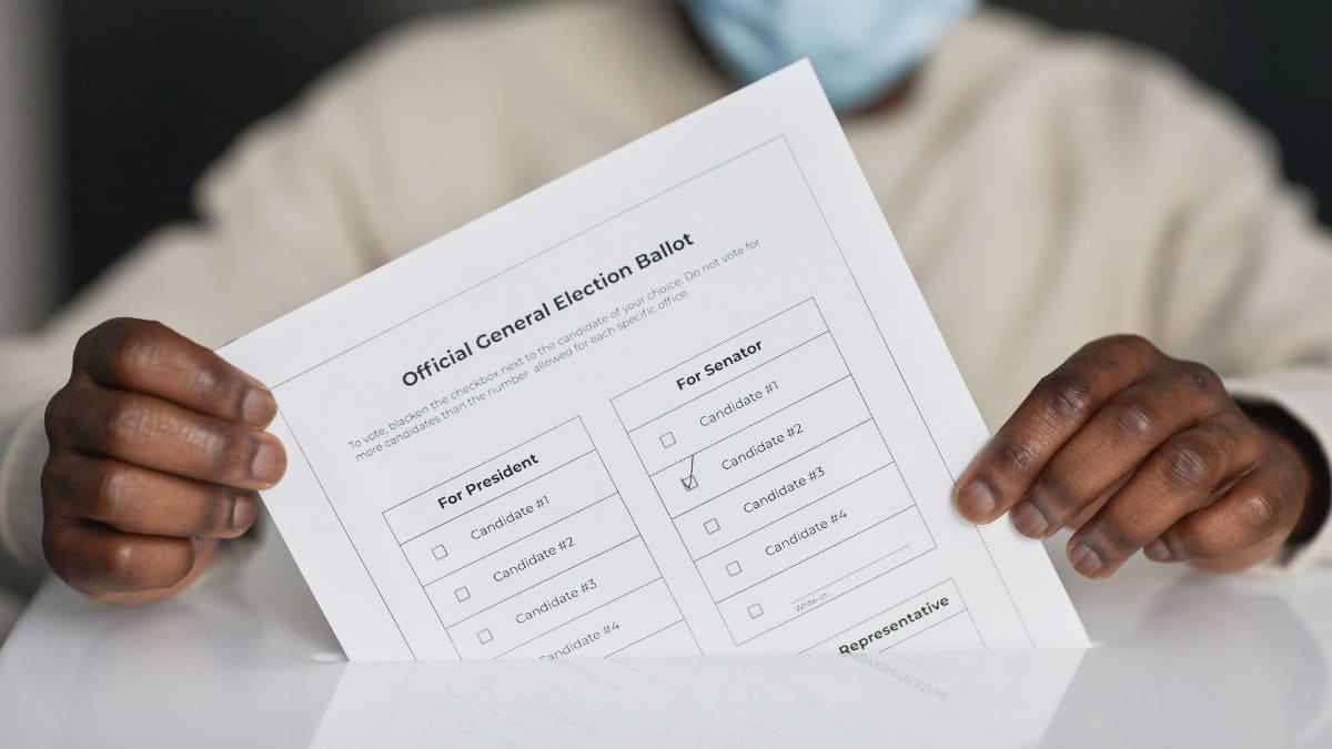 A person wearing a face mask holds an official general election ballot.