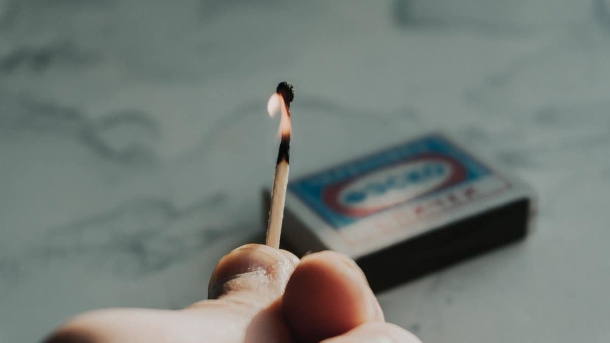 A detailed close-up of a person holding a lit match with a matchbox in the background.