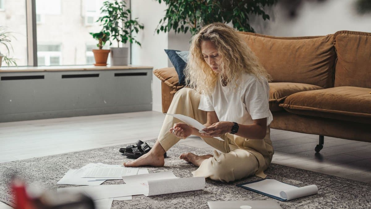 Woman sitting on the floor at home, reviewing paperwork in a relaxed environment.