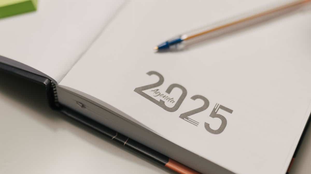 Open 2025 agenda book with a blue pen on a desk, ideal for organization and planning.