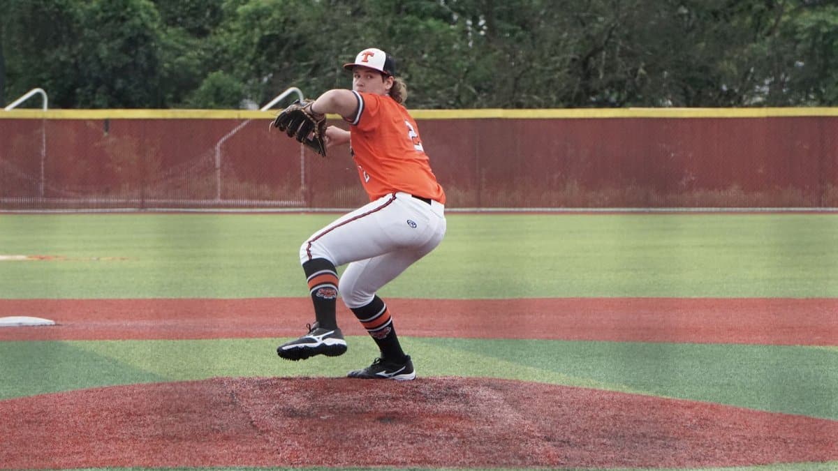 A baseball player in orange jersey pitching on a sunny day.