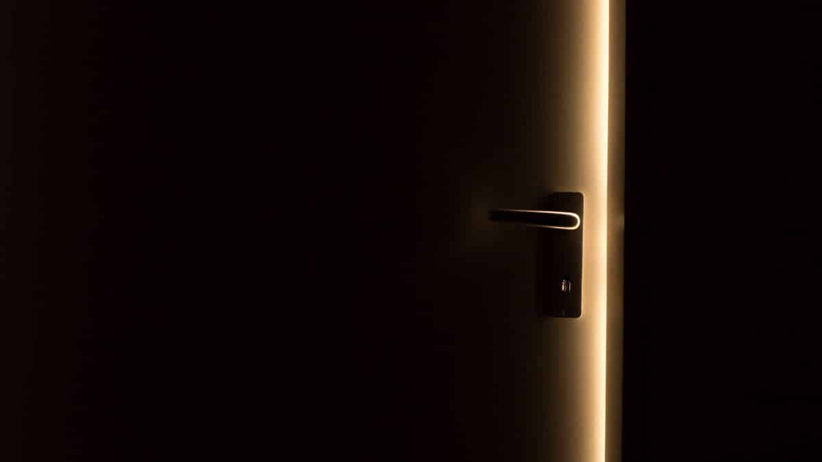 A dark room with a door slightly ajar, revealing a glowing light through the opening.
