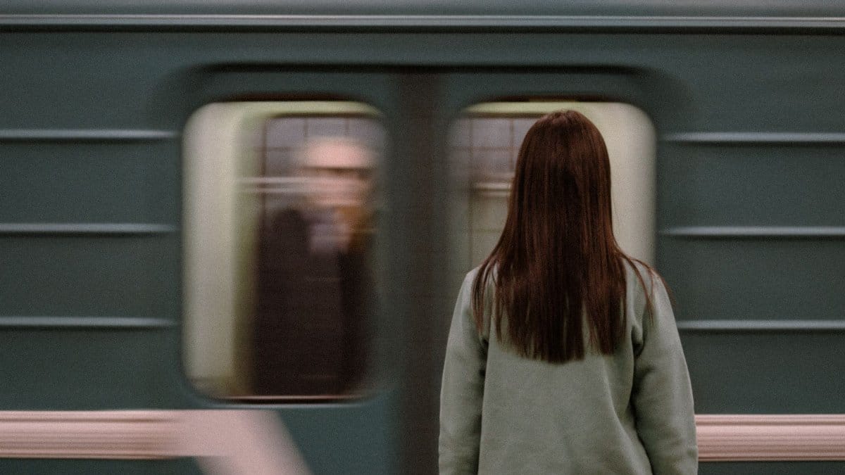 A woman stands on a subway platform watching a train pass by in blurred motion.