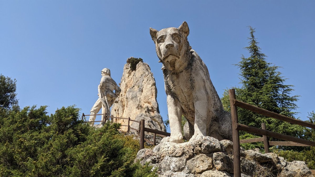 Impressive stone sculptures of a human figure and a large animal under a clear sky.