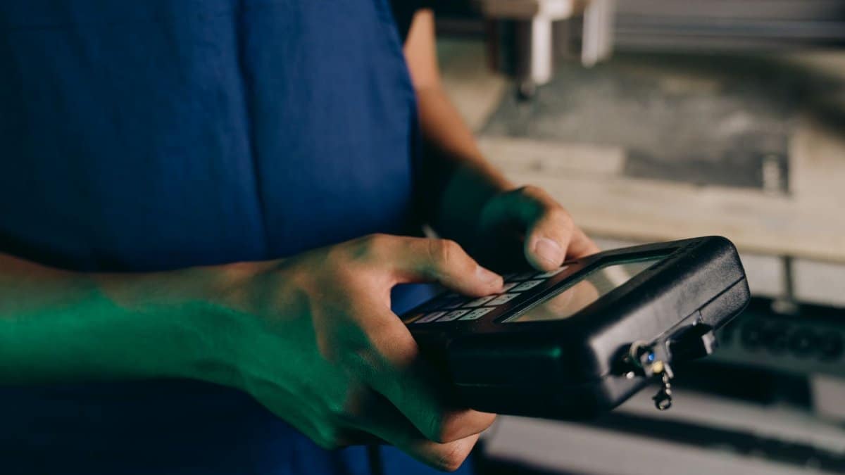 Close-up of technician using a handheld control device in a manufacturing setting.