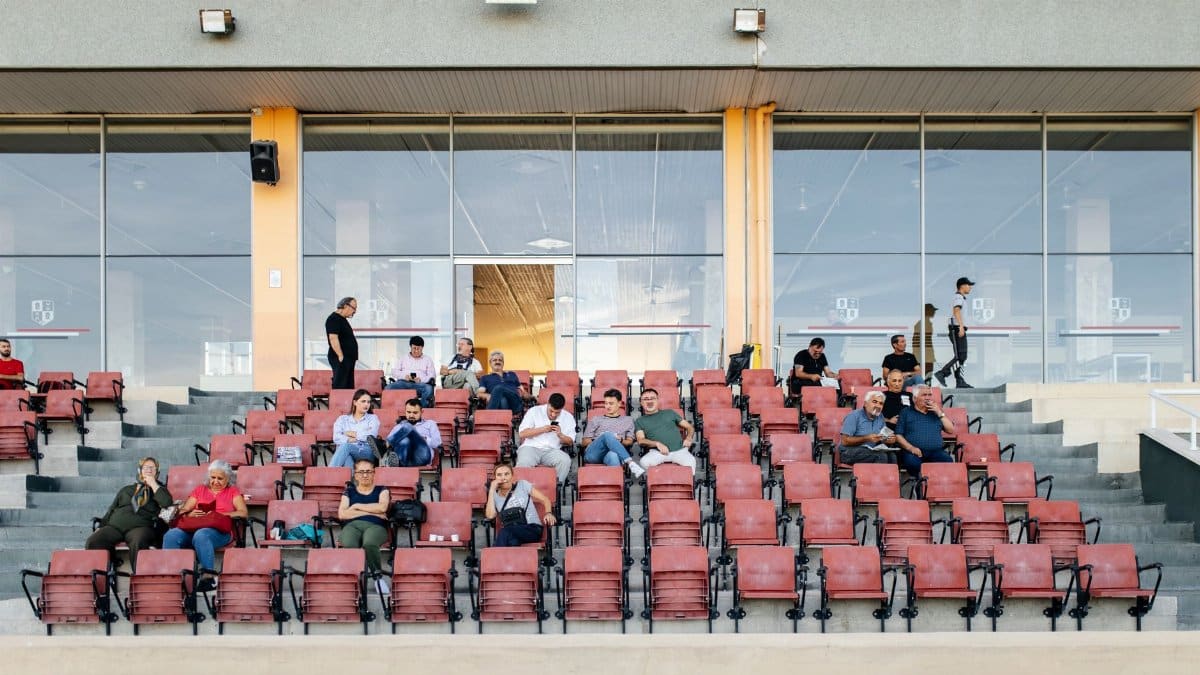 A sparsely occupied stadium grandstand with spectators seated, waiting for an event.