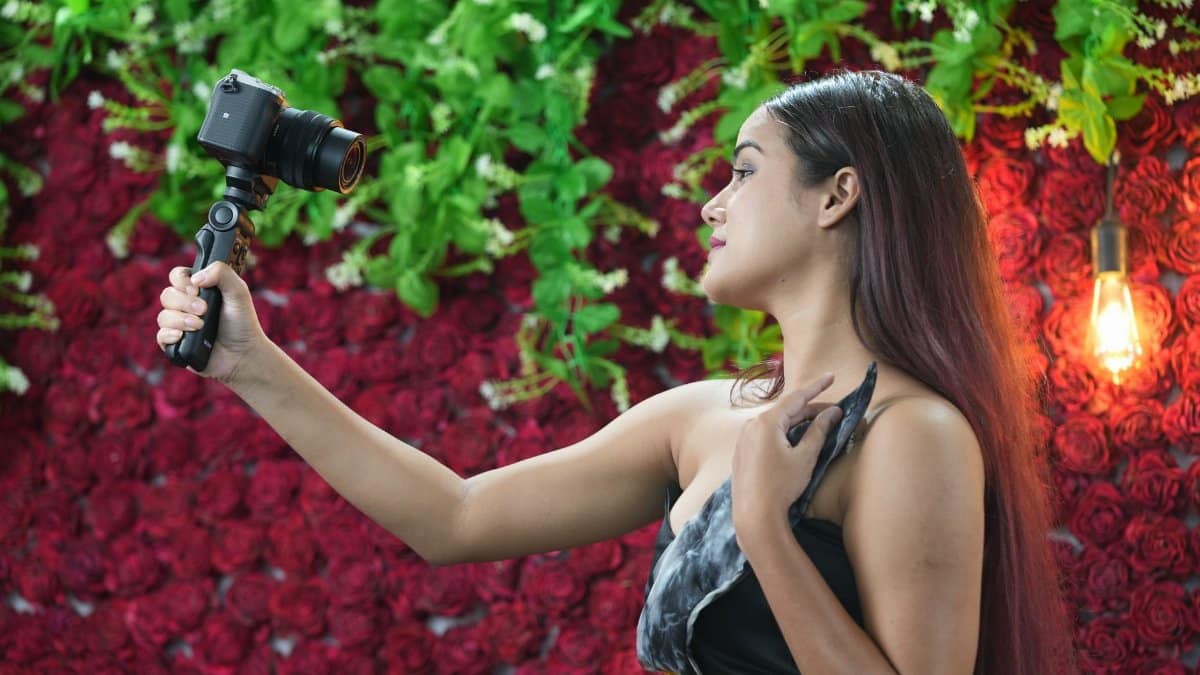 A woman with long hair takes a selfie using a camera against a floral backdrop in Gaya, India.