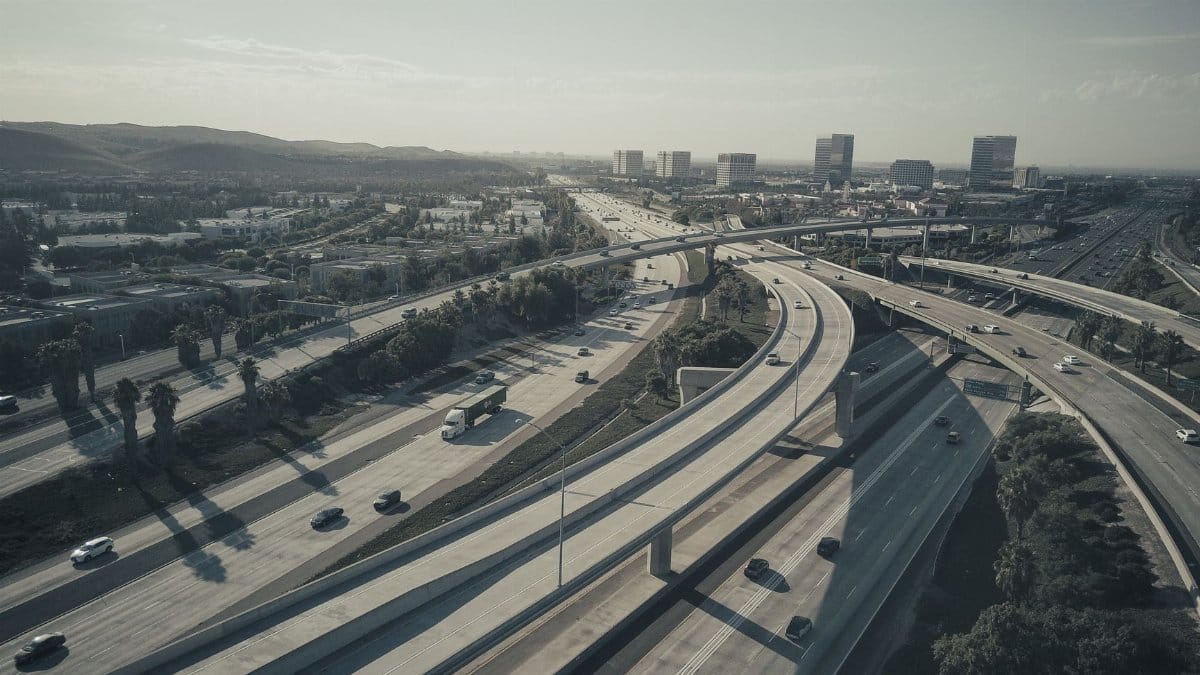 Drone shot of a sprawling highway intersection with moving cars under a cloudy sky.