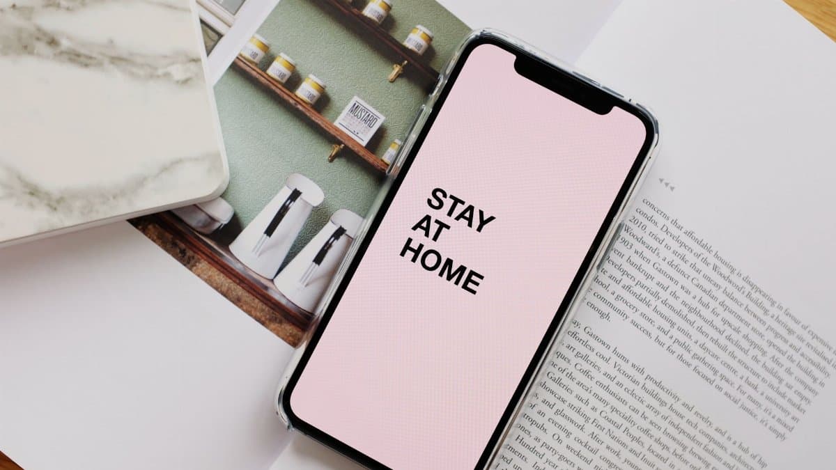 From above of modern cellphone with pale pink screen and STAY AT HOME inscription put on open magazine in apartment during COVID 19 pandemic